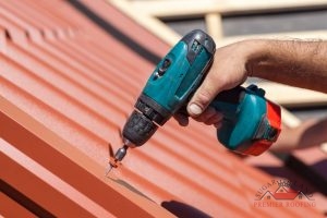 Person with drill fastens metal roof panel in place